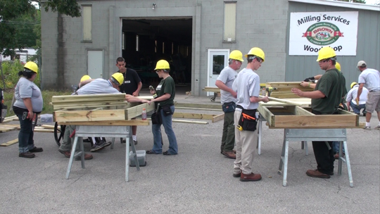 Young people wearing hard hats working with wood outside