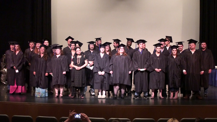 People wearing graduation caps and gowns standing on stage.